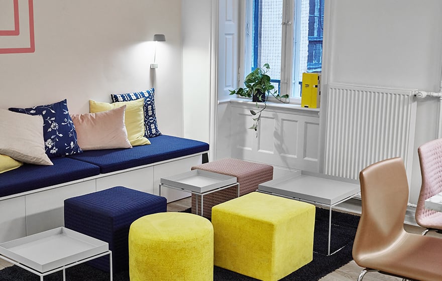 A brightly colored break out space with a wall bench and chairs and office stools.
